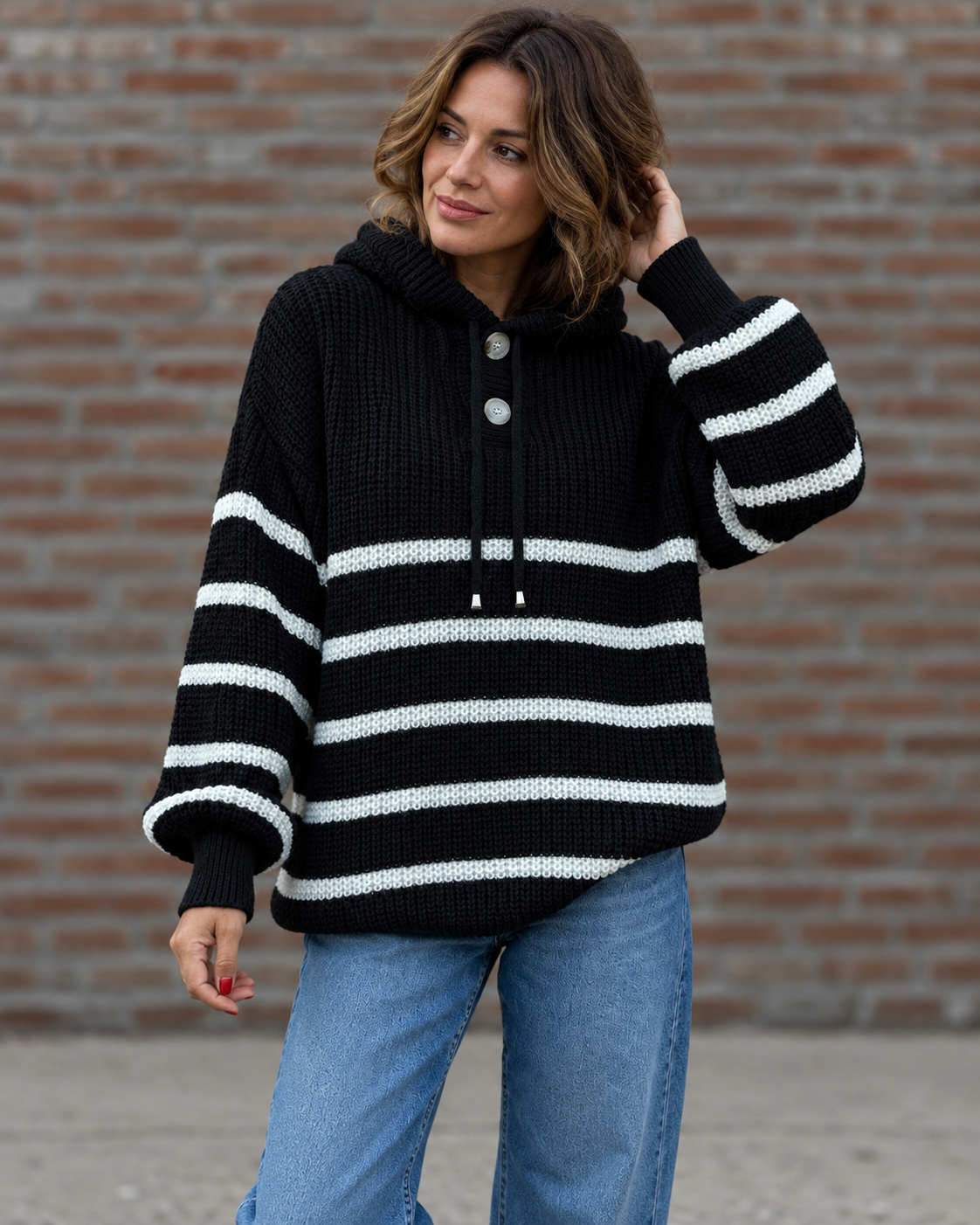 Noélla Montréal — gestreepte hoodie black, tweede volledige modelfoto, pose bij bakstenen muur